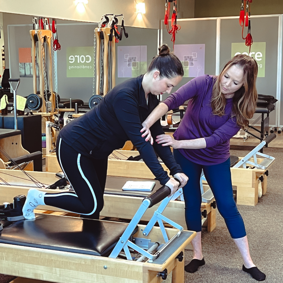 a woman helping another woman exercise on a reformer