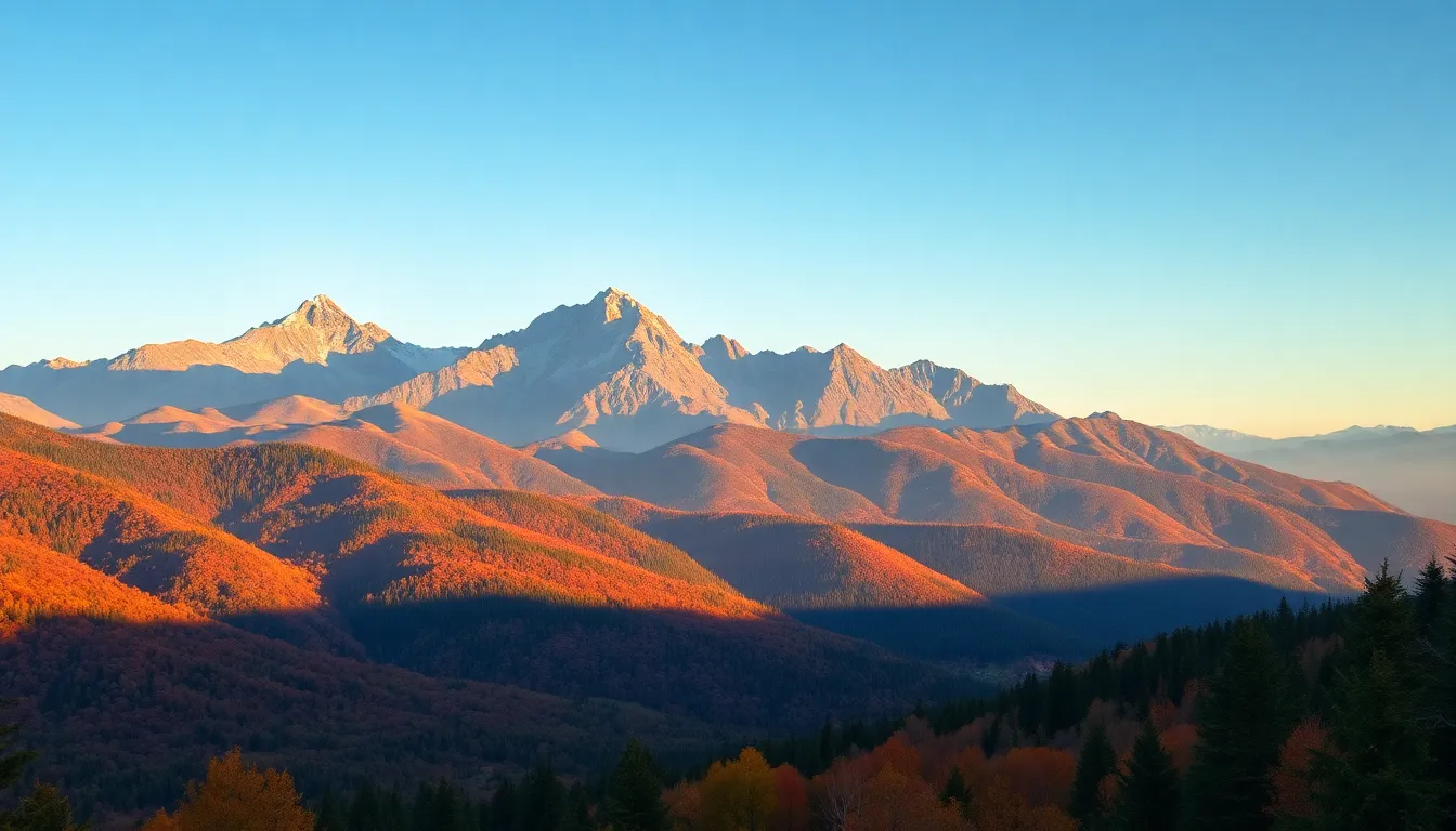 This stunning image captures a majestic mountain landscape during autumn, where vibrant foliage contrasts beautifully against clear blue skies. The valleys are alive with reds and yellows, illuminated by the warm glow of golden hour light. The photograph's depth keeps every detail crisp, from the close trees to the distant mountain peaks, showcasing the breathtaking scale of nature in fall.