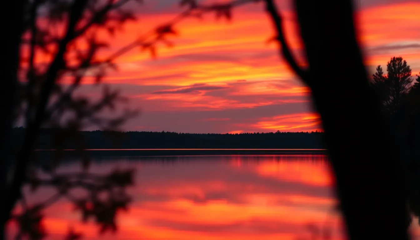 This stunning aerial image captures a serene lake during a vibrant sunset, where dramatic red and orange hues illuminate the sky and reflect beautifully on the water's surface. The shallow depth of field isolates the tranquil lake, enhancing the contrast between warm and cool tones. With silhouettes of trees framing the composition, the horizon line perfectly positioned in the upper third creates a harmonious balance. This peaceful scene evokes a sense of calm and appreciation for nature's beauty.