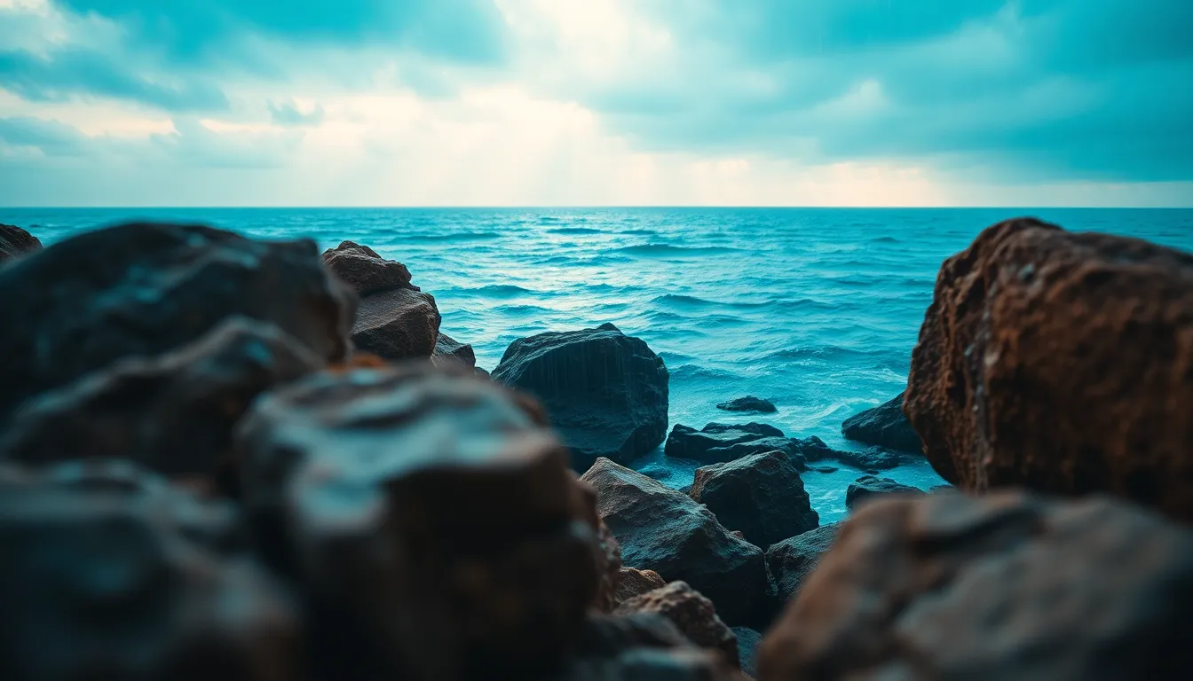 A breathtaking coastal scene unfolds as light rain falls over a vast ocean, the soft sunlight creating a halo effect around the droplets. Bold, textured rocks frame the foreground, leading the eye toward the horizon where the ocean meets the sky. The cinematic color grading enhances the mood, with teal blues and soft oranges merging beautifully. This stunning capture reflects the power of nature and is ideal for ocean and landscape photography.