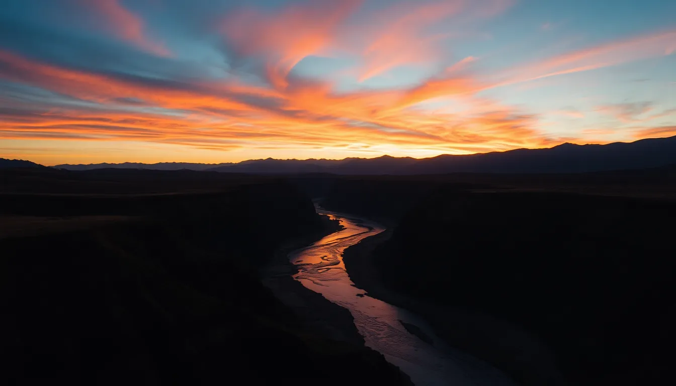 This dramatic landscape photograph captures a river swiftly cutting through a picturesque valley at sunset. The warm colors of the sky create a stunning backdrop, enhancing the silhouettes of distant mountains. Long shadows stretch across the foreground, adding depth to the scene. The dynamic angle captures the river's movement, inviting the viewer to explore the natural magic of this serene moment.