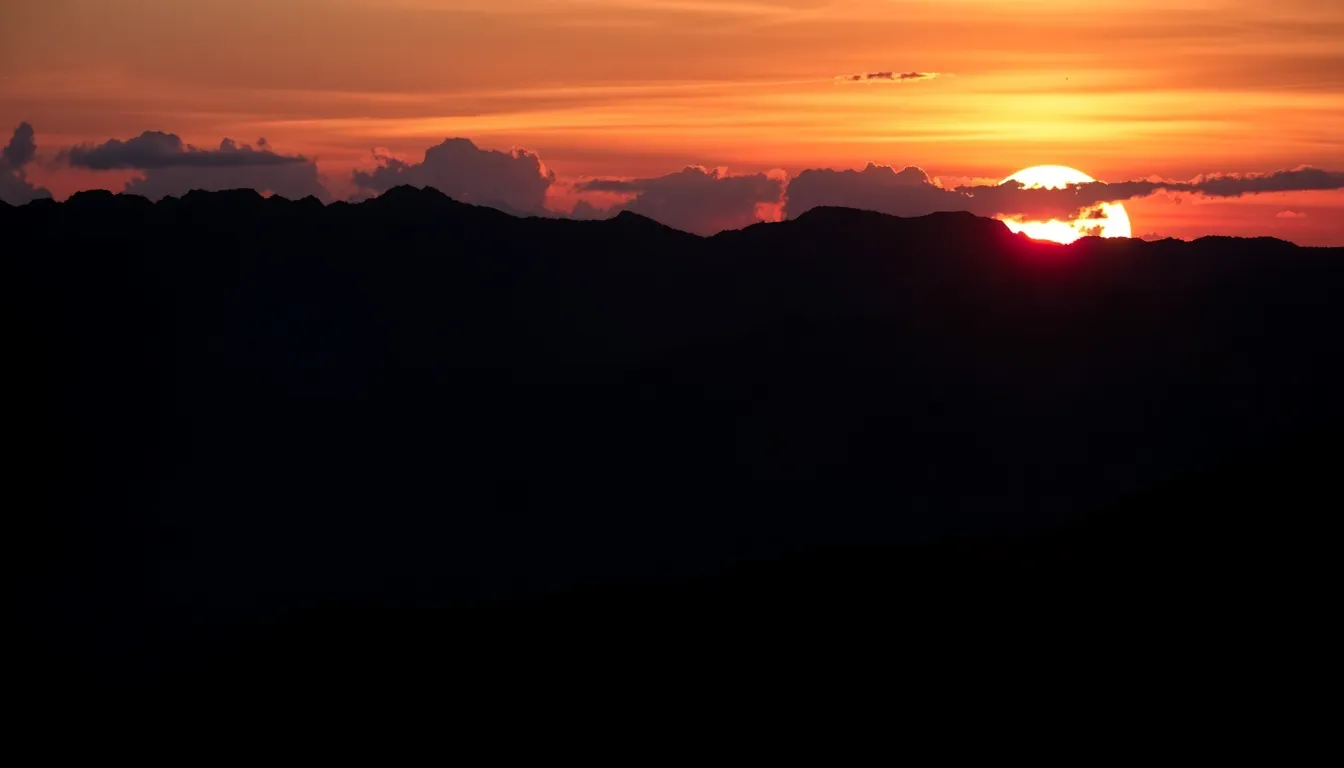 Dramatic Sunset Behind Mountain Range This dramatic image showcases a breathtaking sunset behind a silhouetted mountain range, where deep blues meet fiery oranges in the sky. The rugged peaks are crisply detailed, highlighting the textural contrasts against the vibrant clouds. The hyperfocal depth of field captures everything from the foreground to the distant horizon in sharp focus, enhancing the grandeur of the scene. This composition employs leading lines formed by the mountains, effectively guiding the viewer toward the radiant sky.