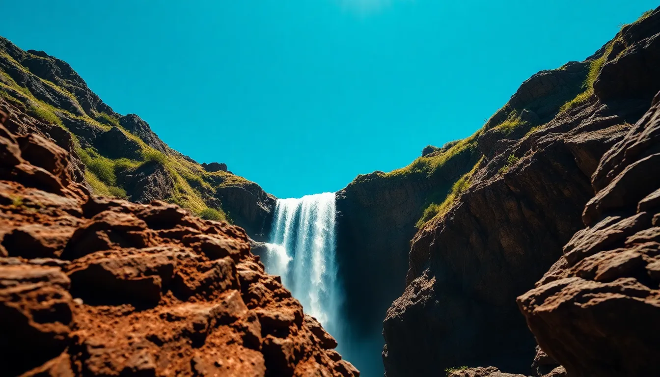A breathtaking waterfall pours down a rocky hillside, set against a vibrant blue sky. Bright daylight creates a striking contrast, bringing out vivid colors in the lush greenery and the sparkling water. The composition utilizes a rule of thirds approach, effectively drawing the eye to the waterfall, which serves as a focal point in the scene. With sharp details captured from the foreground to the background, this image beautifully showcases the splendor of nature.